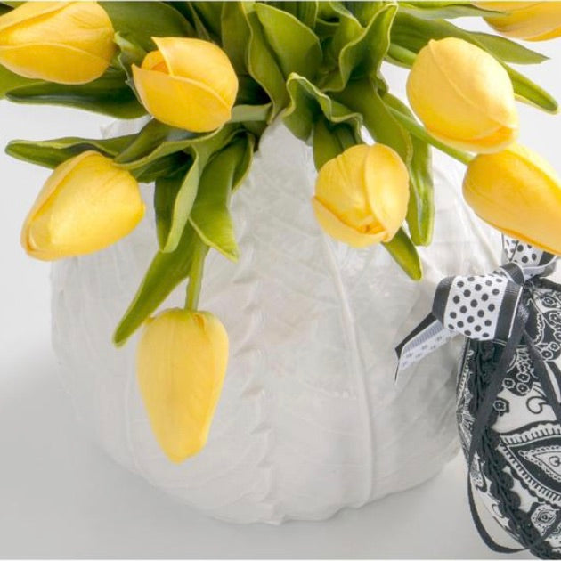 A bundle of light yellow tulips with green leaves, arranged in a white container, adorned with a paper bow.