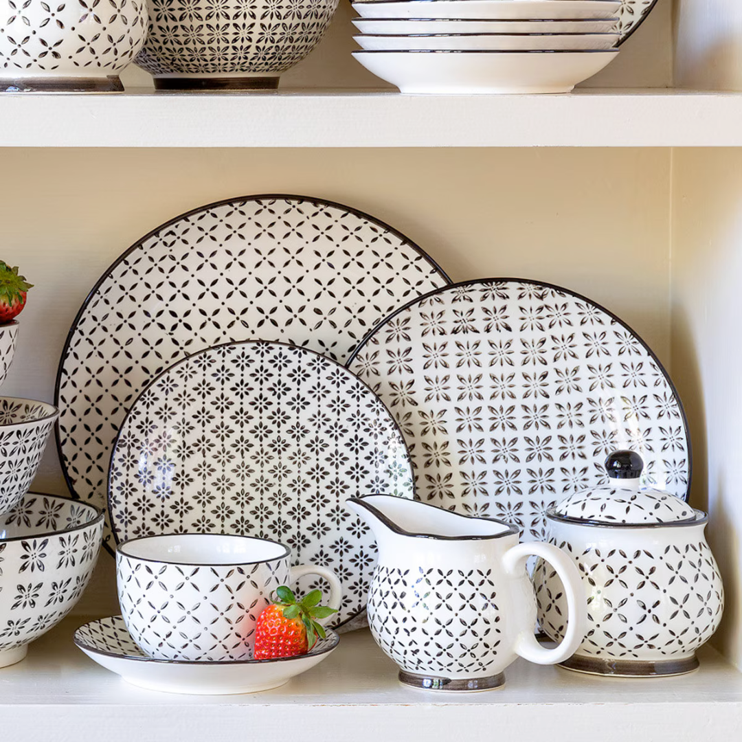 Patterned ceramic dishes including plates, bowls, and a pitcher on a shelf.
