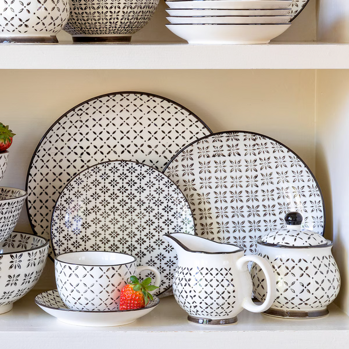 Patterned ceramic dishes including plates, bowls, and a pitcher on a shelf.