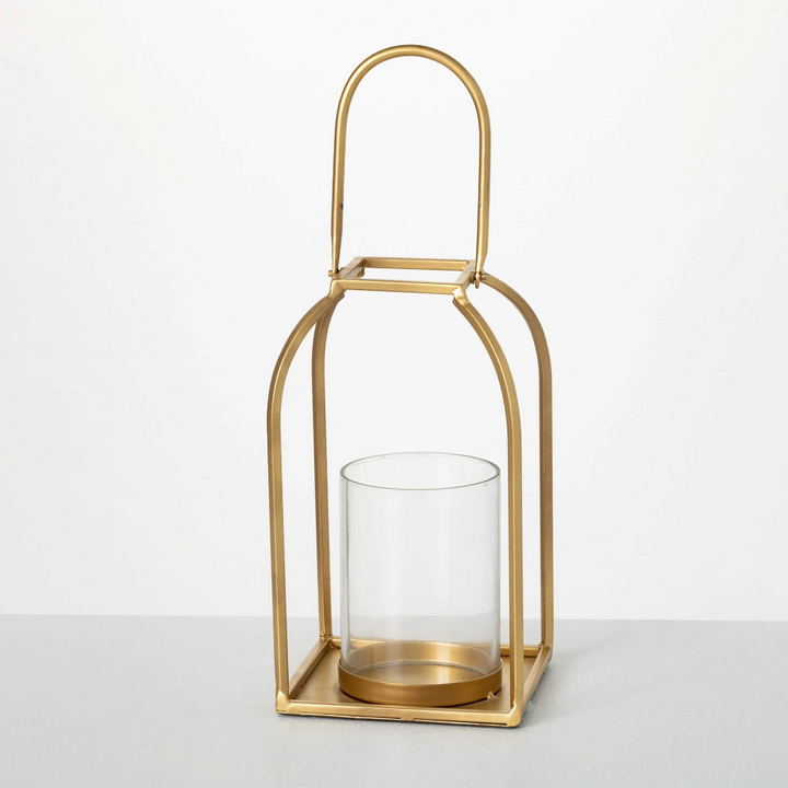 A brushed gold metal lantern candle holder with a clear glass hurricane liner.