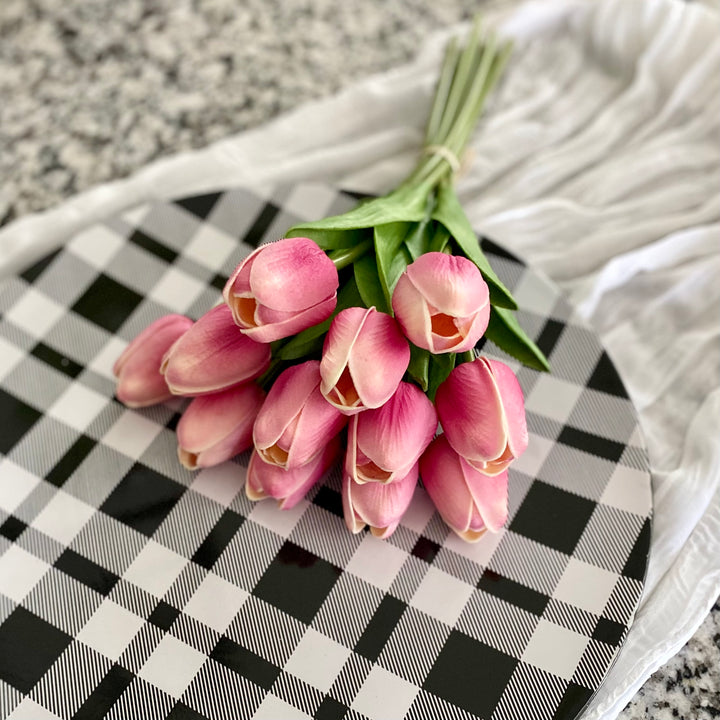 A bundle of artificial mauve tulips tied with a paper bow, placed on a black and white checkered surface.