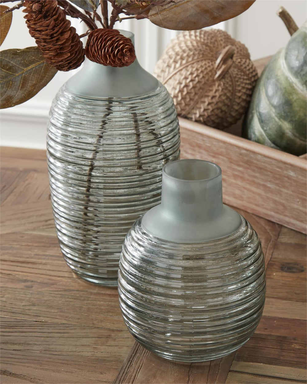 Two ribbed glass vases on a wooden surface with decorative elements in the background.