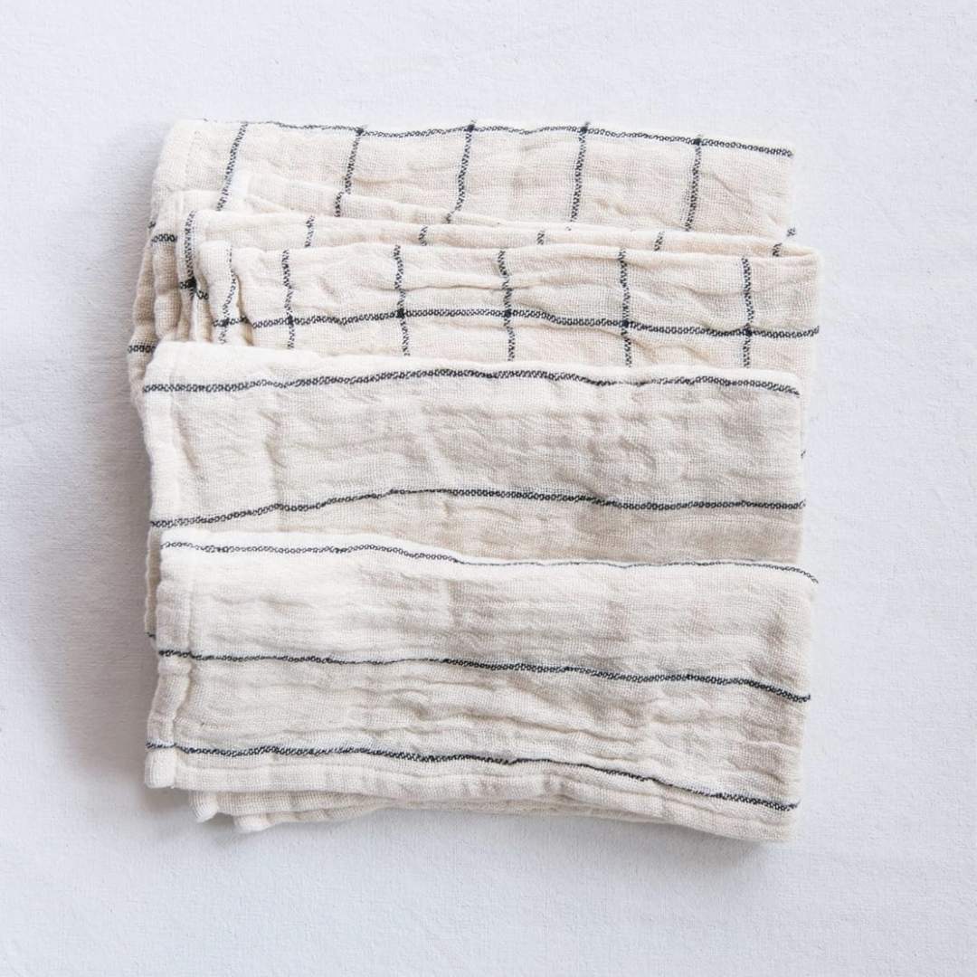 A set of four folded striped cotton napkins in beige and black colors with a plaid pattern on a white background.