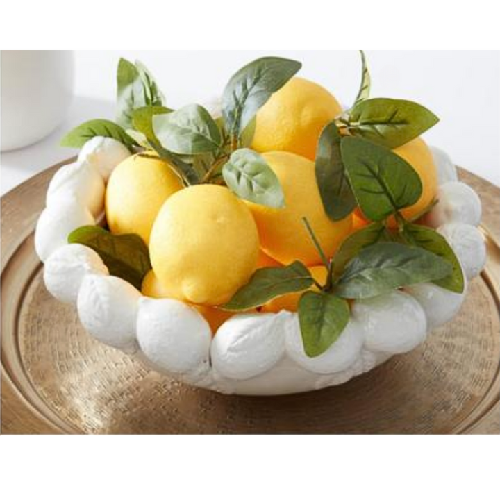 Artificial lemons with green leafy foliage in a white ceramic bowl