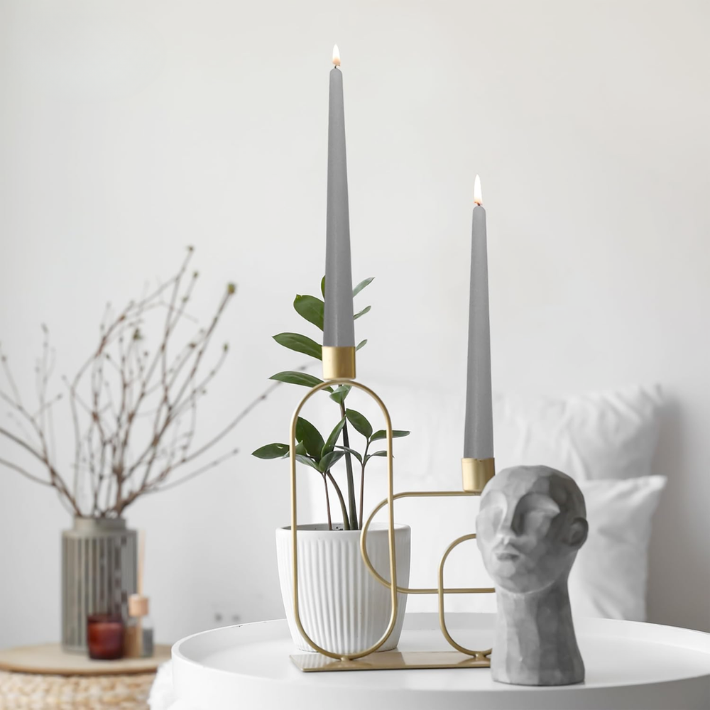 Decorative setup with gray taper candles, plant, and sculpture on a white surface.