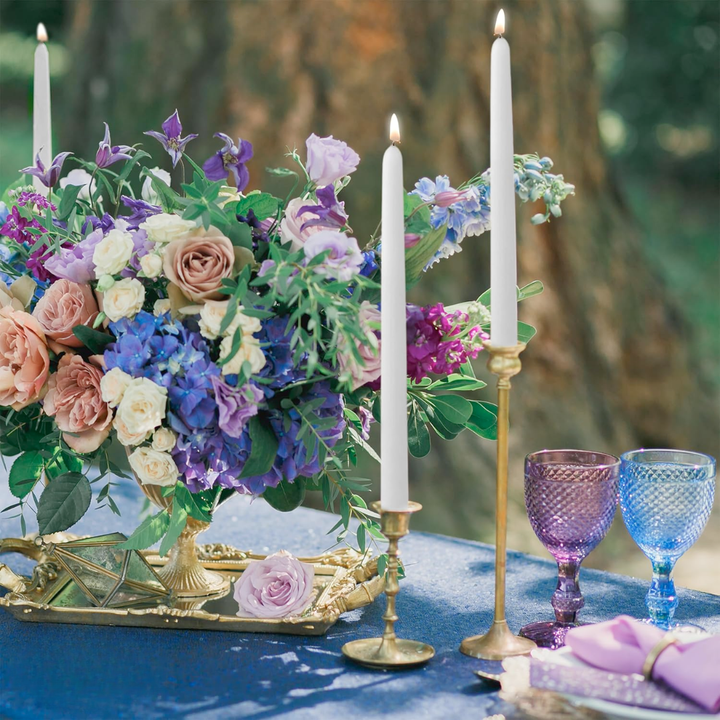 Decorative table setting with flowers, candles, and colorful glasses on a blue surface.