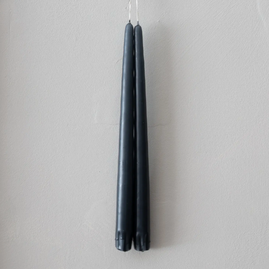 Two long charcoal gray taper candles hanging side by side against a plain light gray wall.