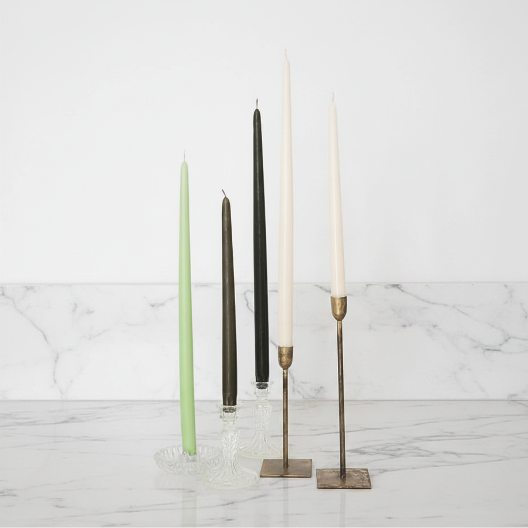 A selection of 12-inch taper candles in ivory and gray, displayed in various candle holders against a neutral background.