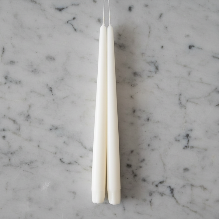 Two tall, slender ivory taper candles hanging side by side against a plain light gray wall.
