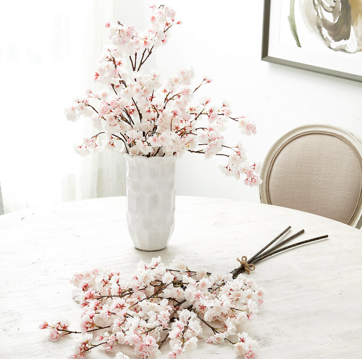 White vase with pink artificial flowers on a white tablecloth