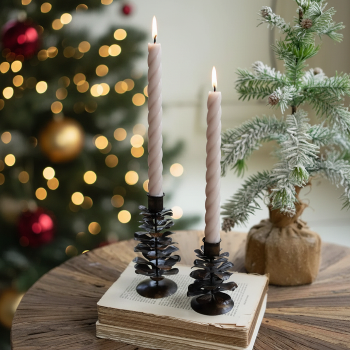 Two lit candles on pinecone candle holders with a Christmas tree in the background