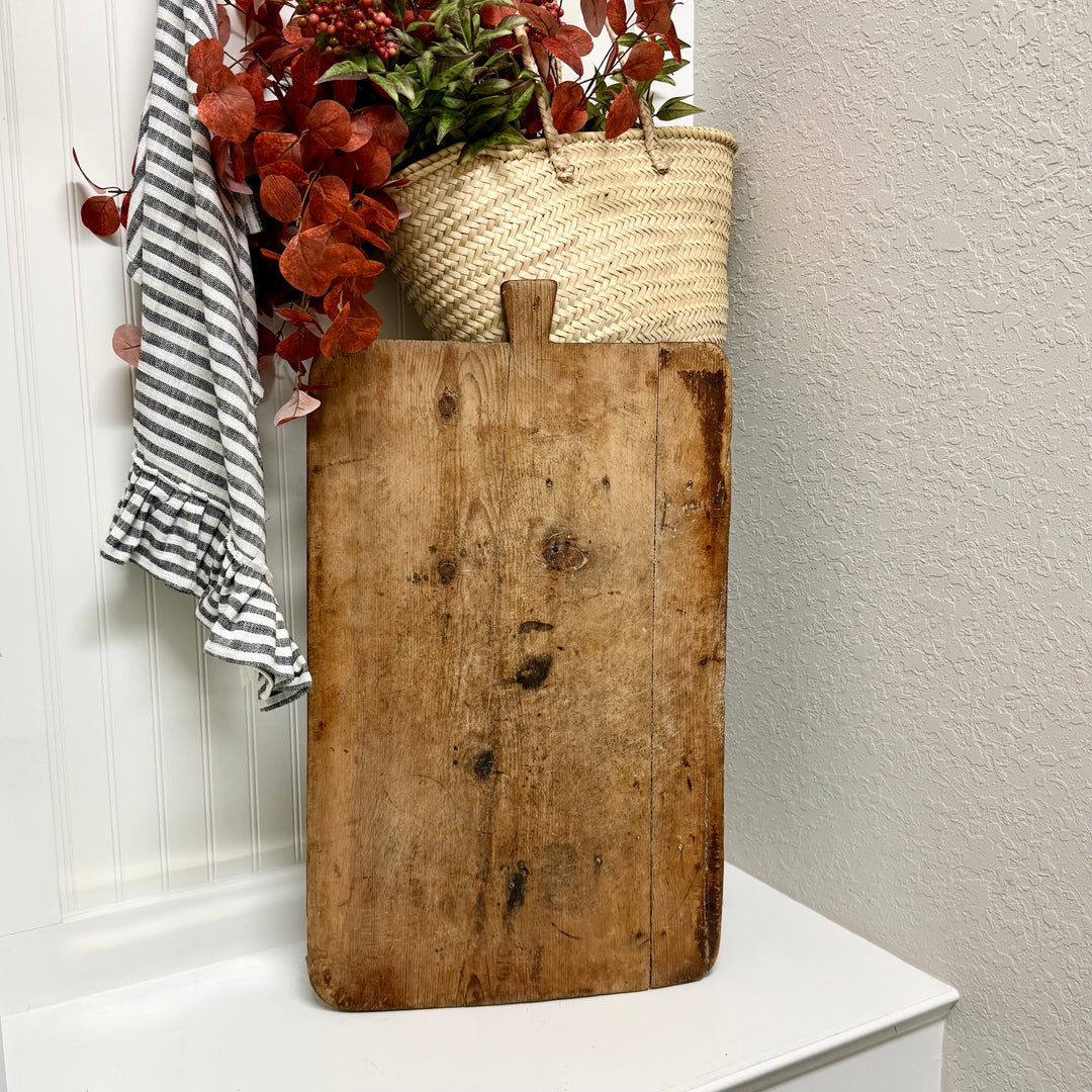 Vintage wooden cutting board with a woven basket and red leaves on a white surface.