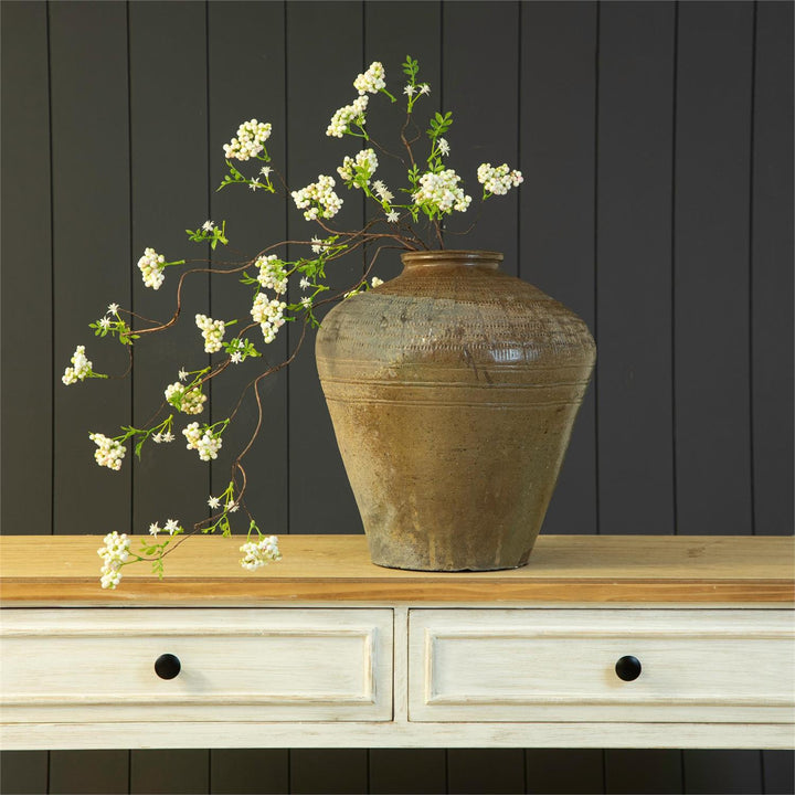 Decorative vase with white flowers on a wooden surface against a dark paneled wall.
