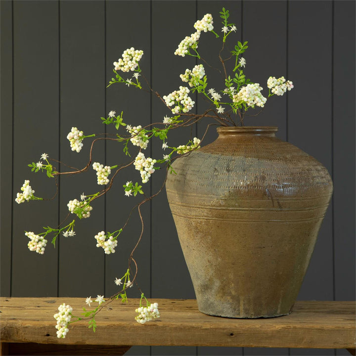 Decorative vase with white flowers on a wooden surface against a dark wooden panel background