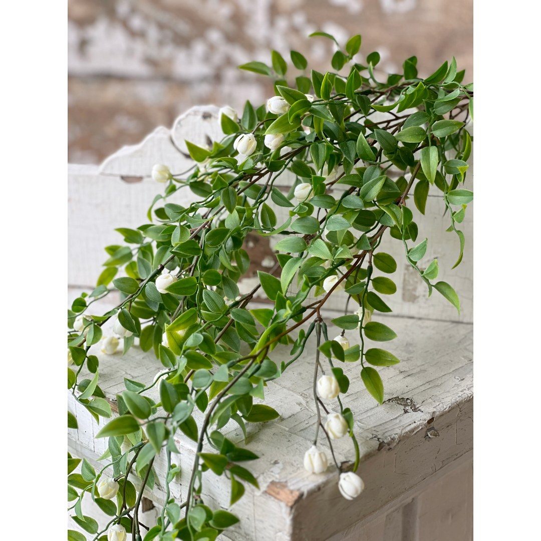 Artificial green vine with white flowers on a wooden surface