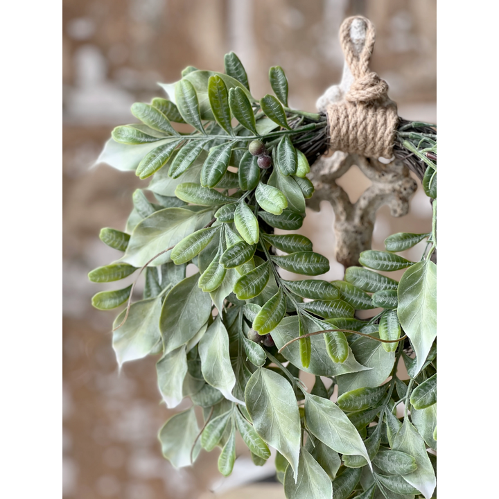 Decorative wreath with green leaves and a rustic wooden hook on a blurred background