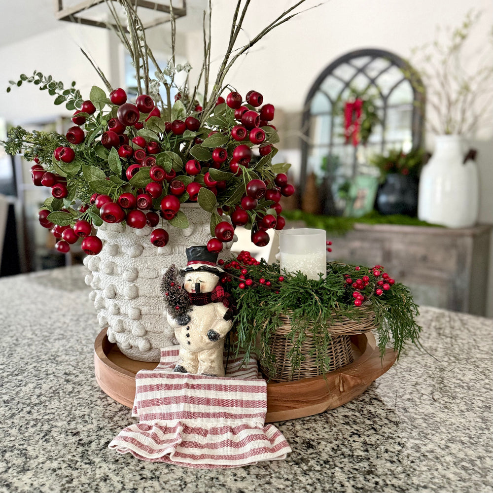 Decorative arrangement with berries, a teddy bear, and a candle on a table.