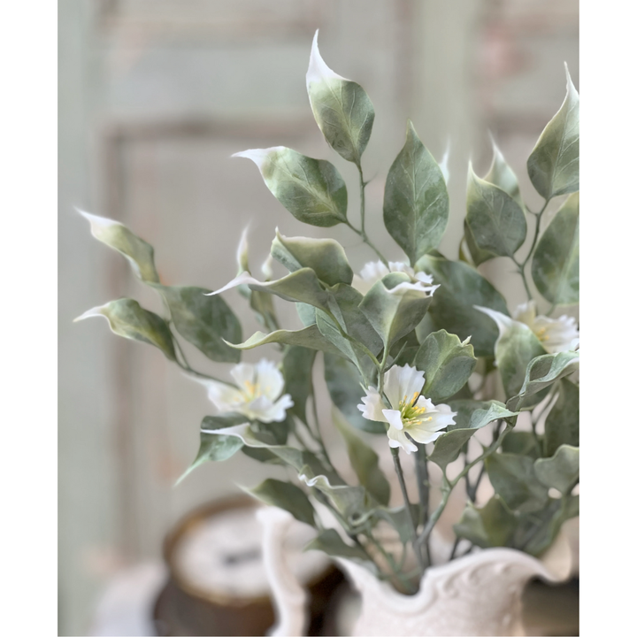 Artificial greenery with white flowers in a decorative vase against a neutral background