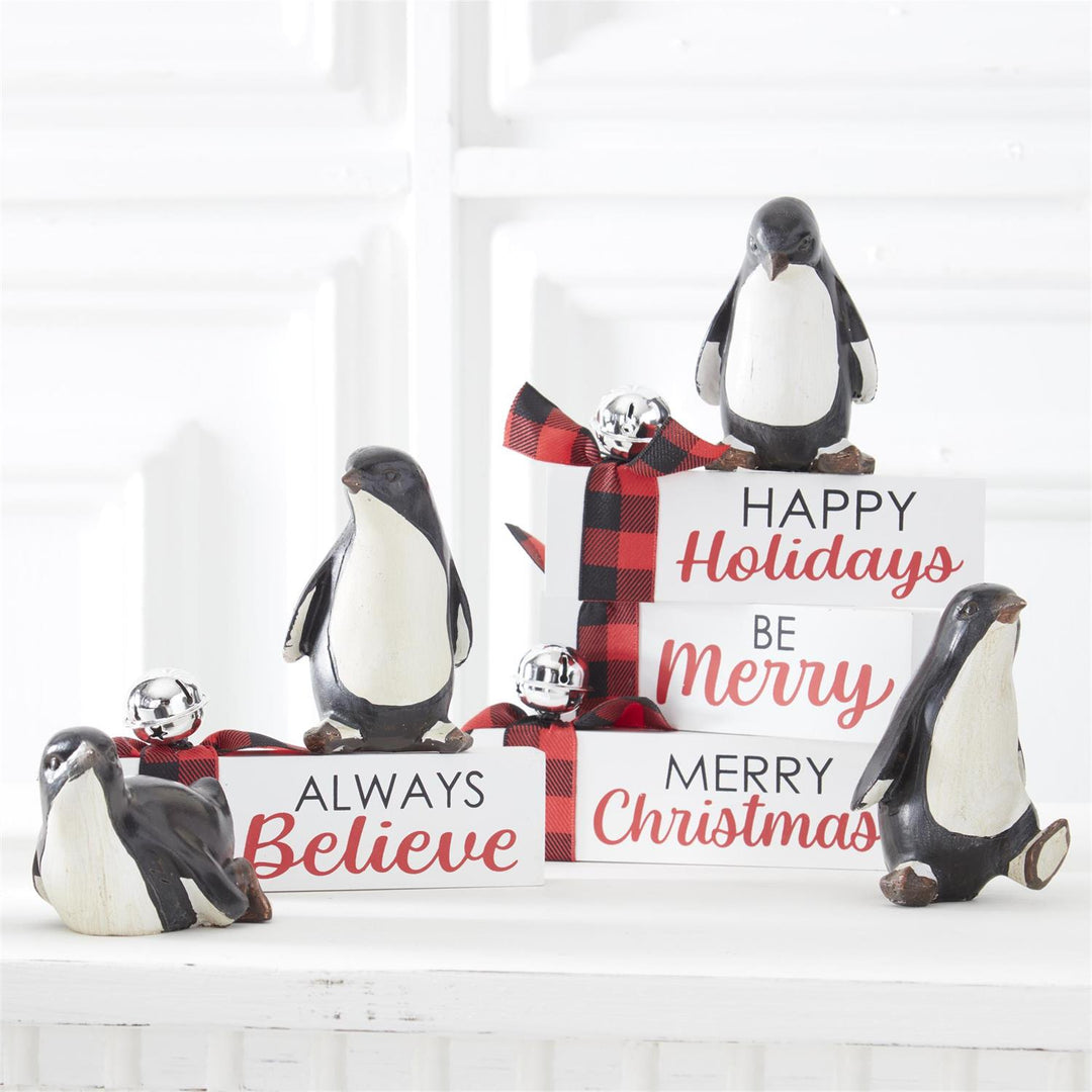 Decorative penguin figurines with Christmas-themed signs on a white surface.