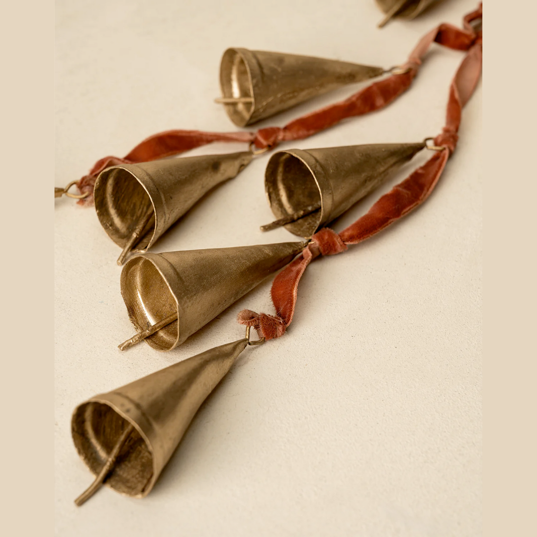Decorative string of brass bells with red ribbons on a beige background
