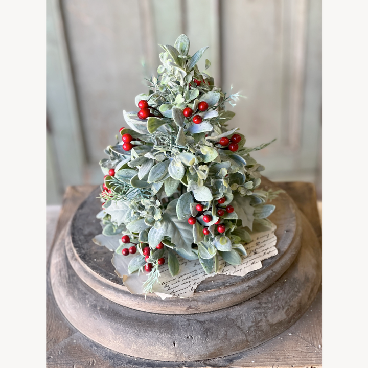 Decorative Christmas tree with green leaves and red berries on a wooden stand.