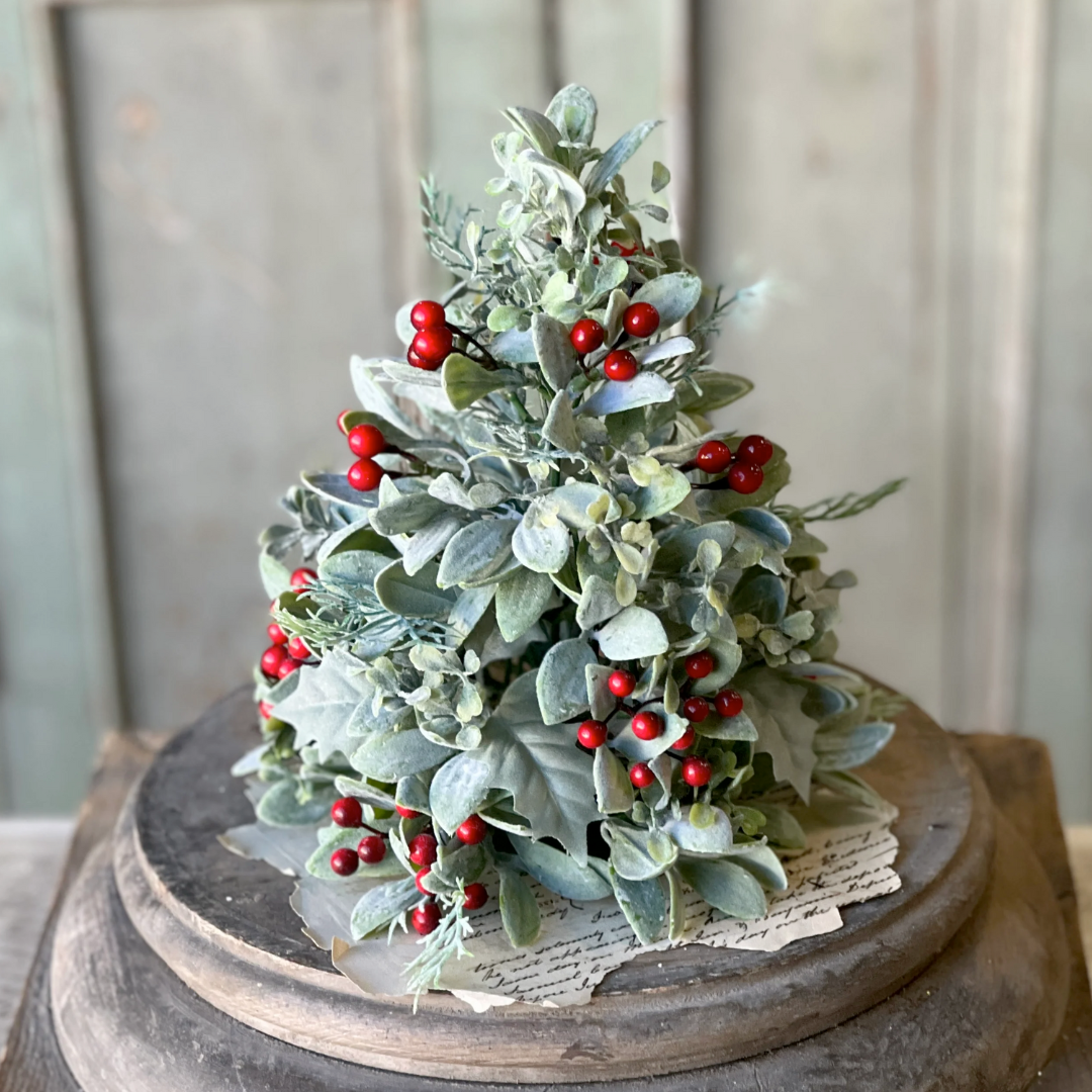 Decorative Christmas tree with green leaves and red berries on a wooden stand.