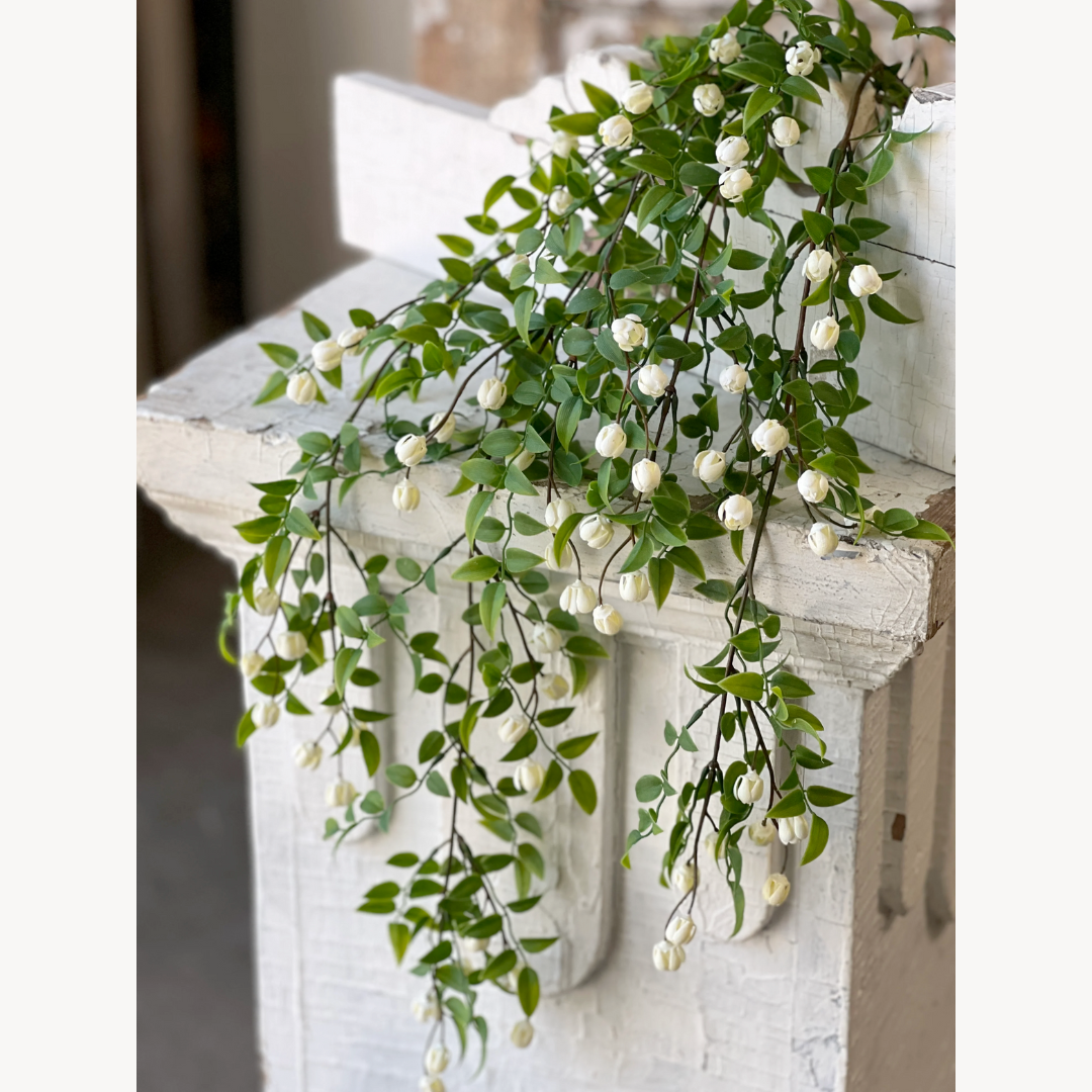 Artificial greenery with white flowers on a decorative fireplace mantle.
