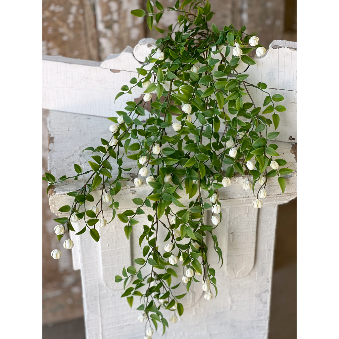 Artificial green vine with white flowers on a decorative white pedestal