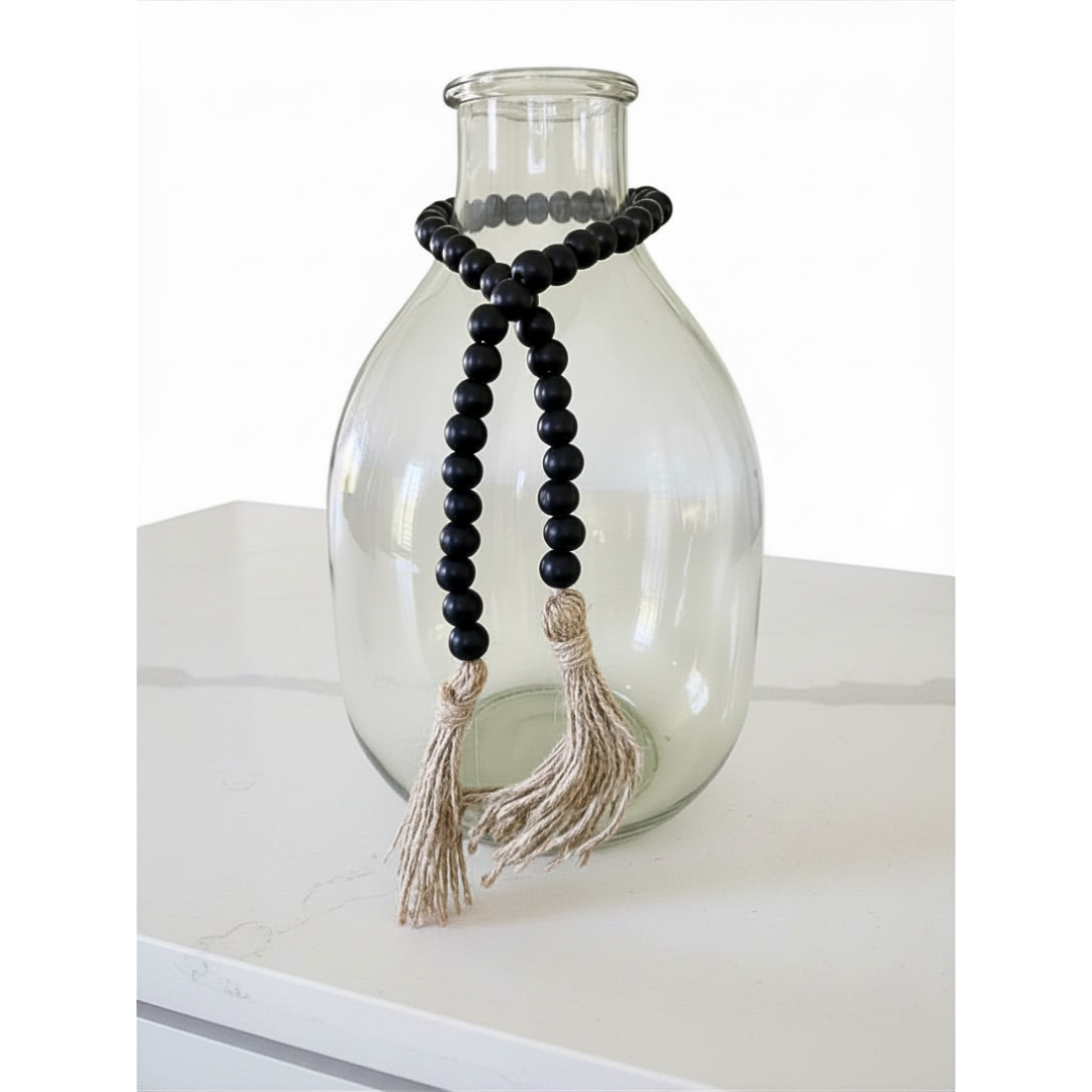 Glass vase with black beaded garland and tassels on a white surface