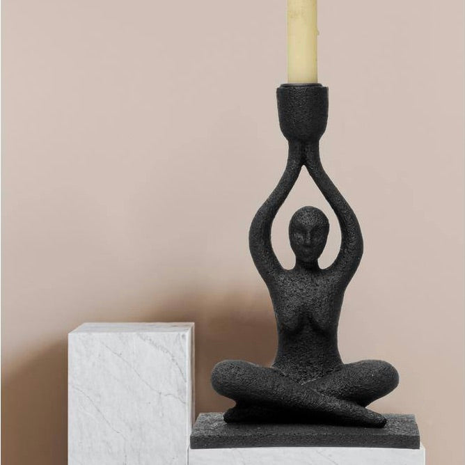 A black Lotus Pose Candle Holder made of polyresin, featuring a figure in a cross-legged pose with hands raised, holding a candle.