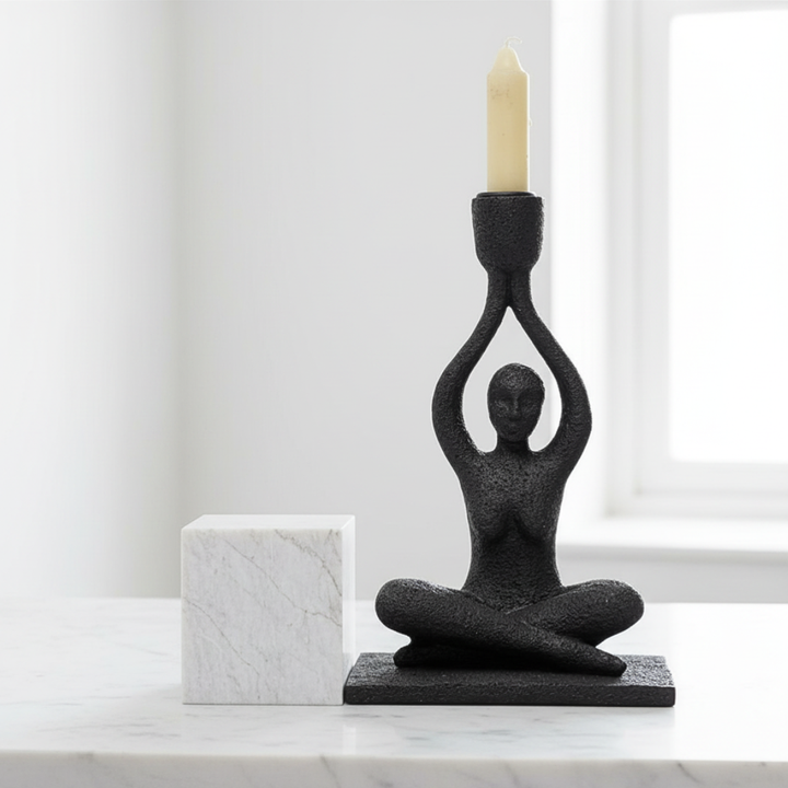 Black abstract candle holder in the shape of a person on a marble surface with a white background