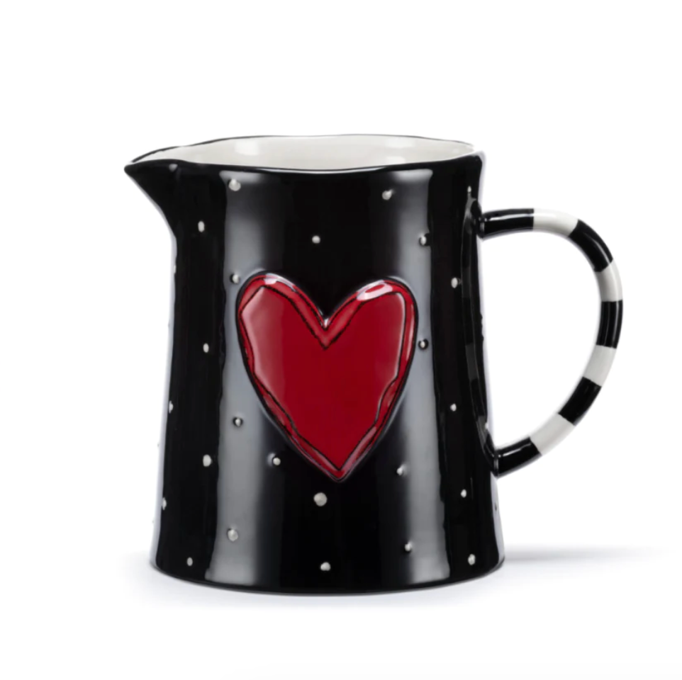 A black stoneware pitcher with white polka dots and a red embossed heart, featuring a striped handle.