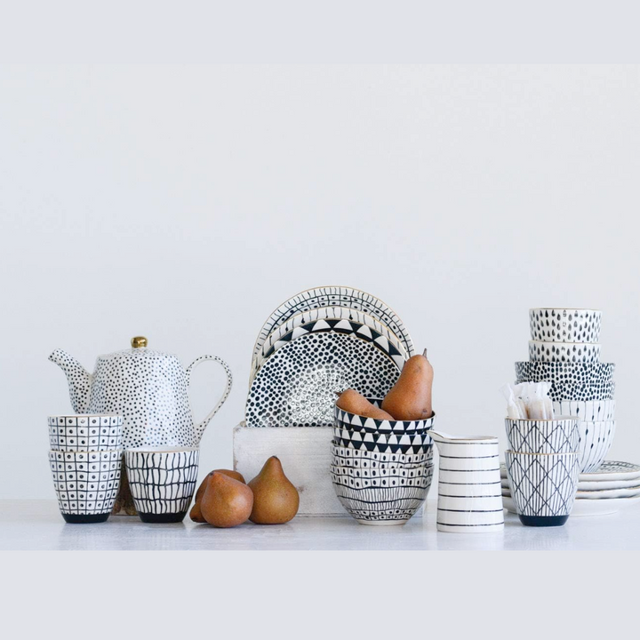 A set of four black and white glitzy stoneware bowls with gold rims, along with a teapot and some fruit, displayed on a white surface.