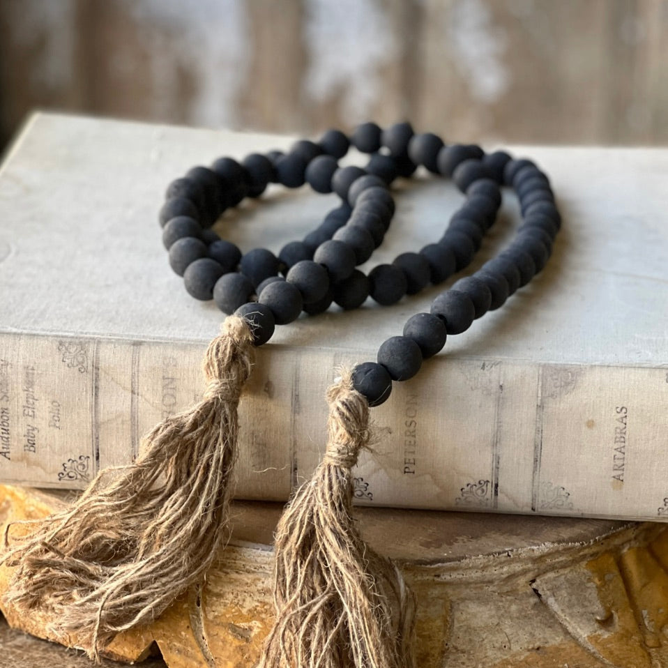 A black bead garland with tassels placed on an open book, with the beads hanging down over the edges of the pages.