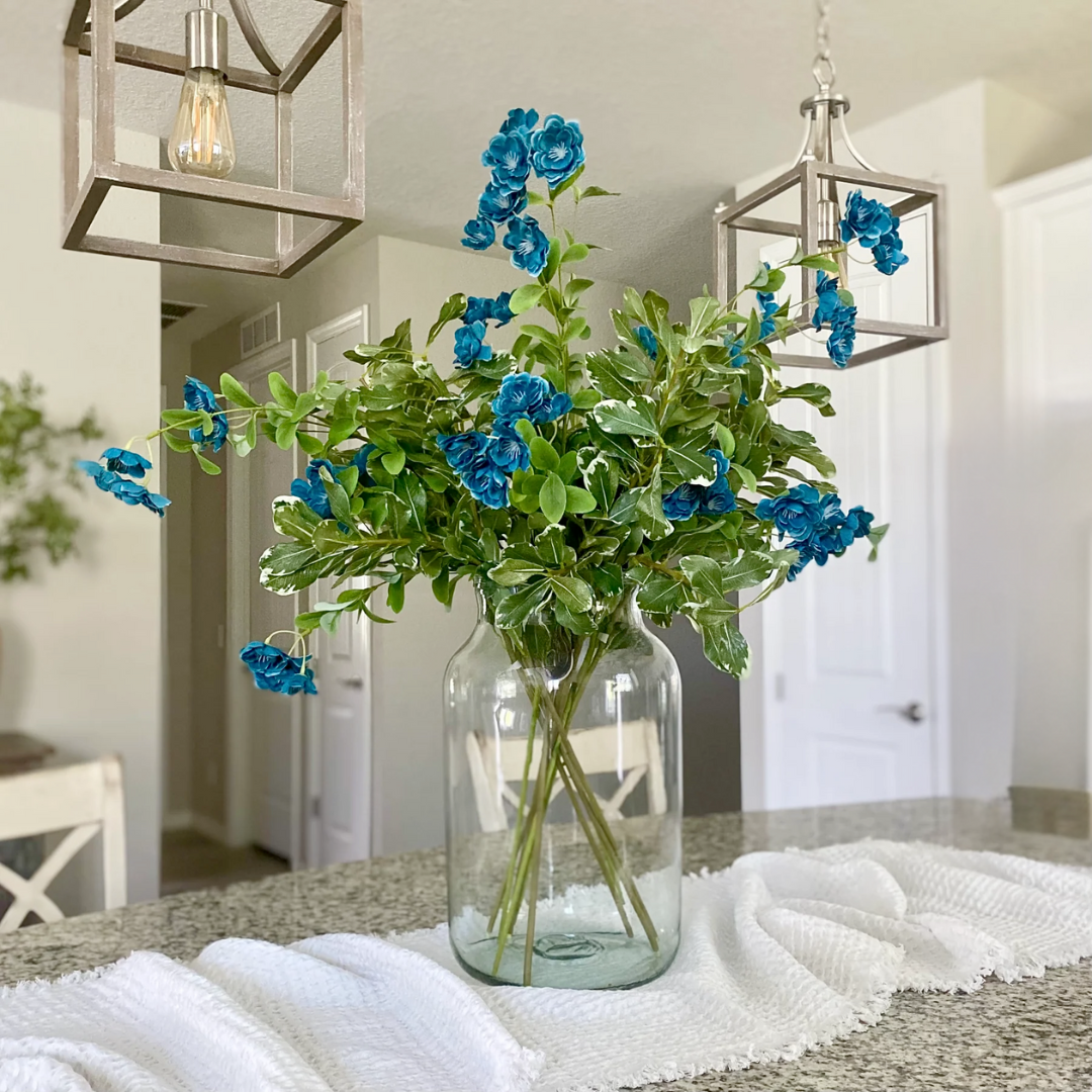 Clear glass vase with blue flowers on a table in a home setting
