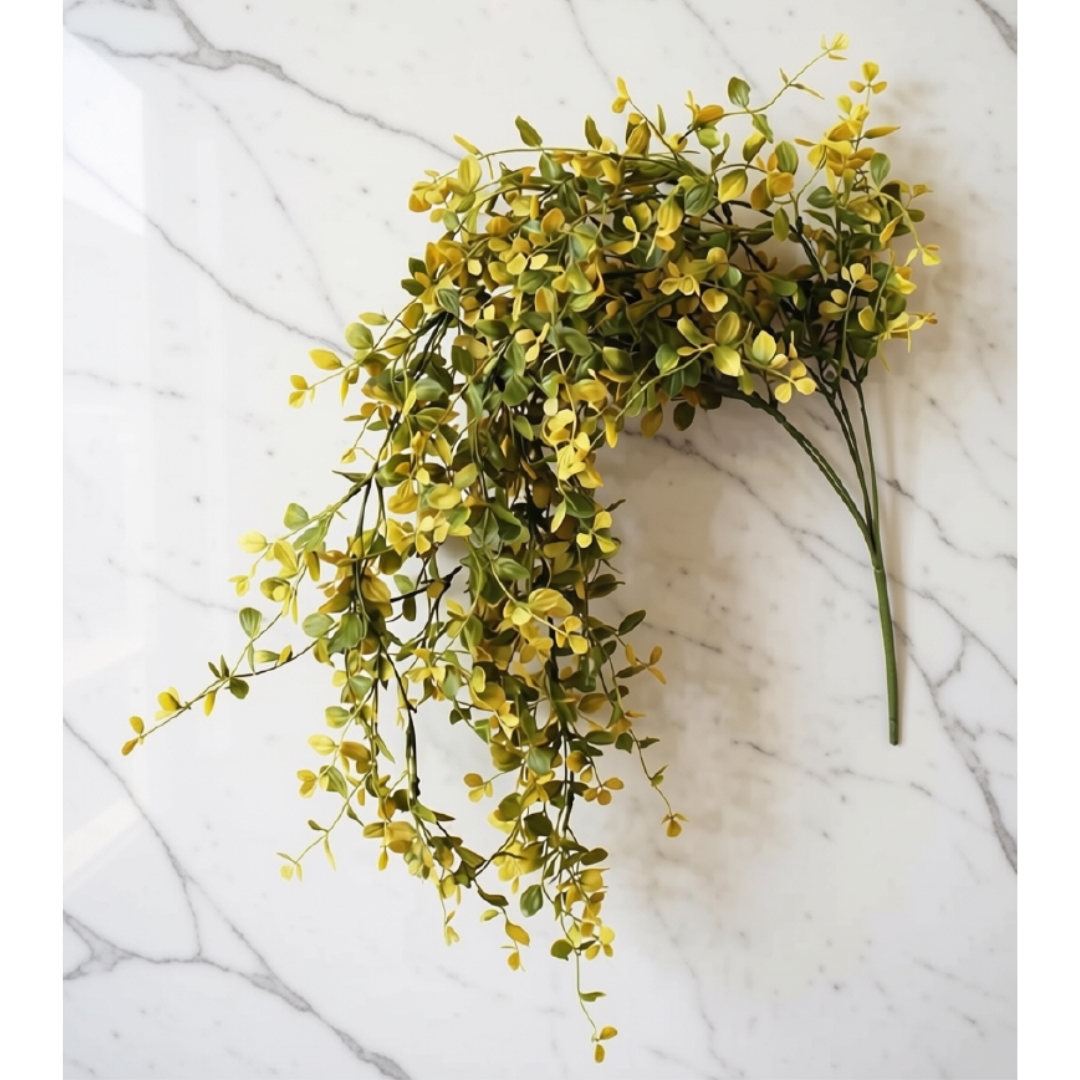 A bunch of artificial yellow-green foliage stems arranged on a white marble surface.