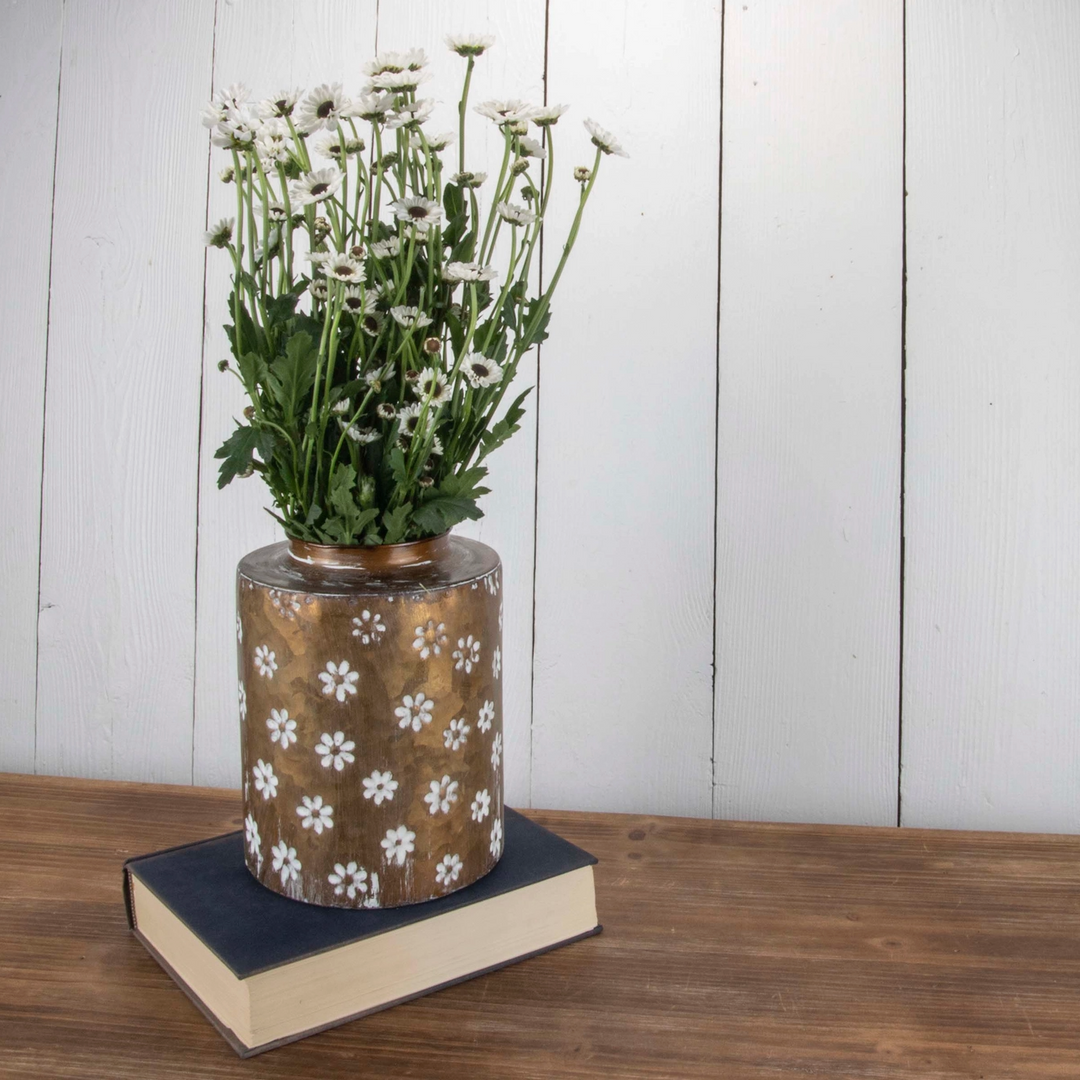 A brass vase with a floral pattern, displaying white flowers, placed on a book on a wooden surface.