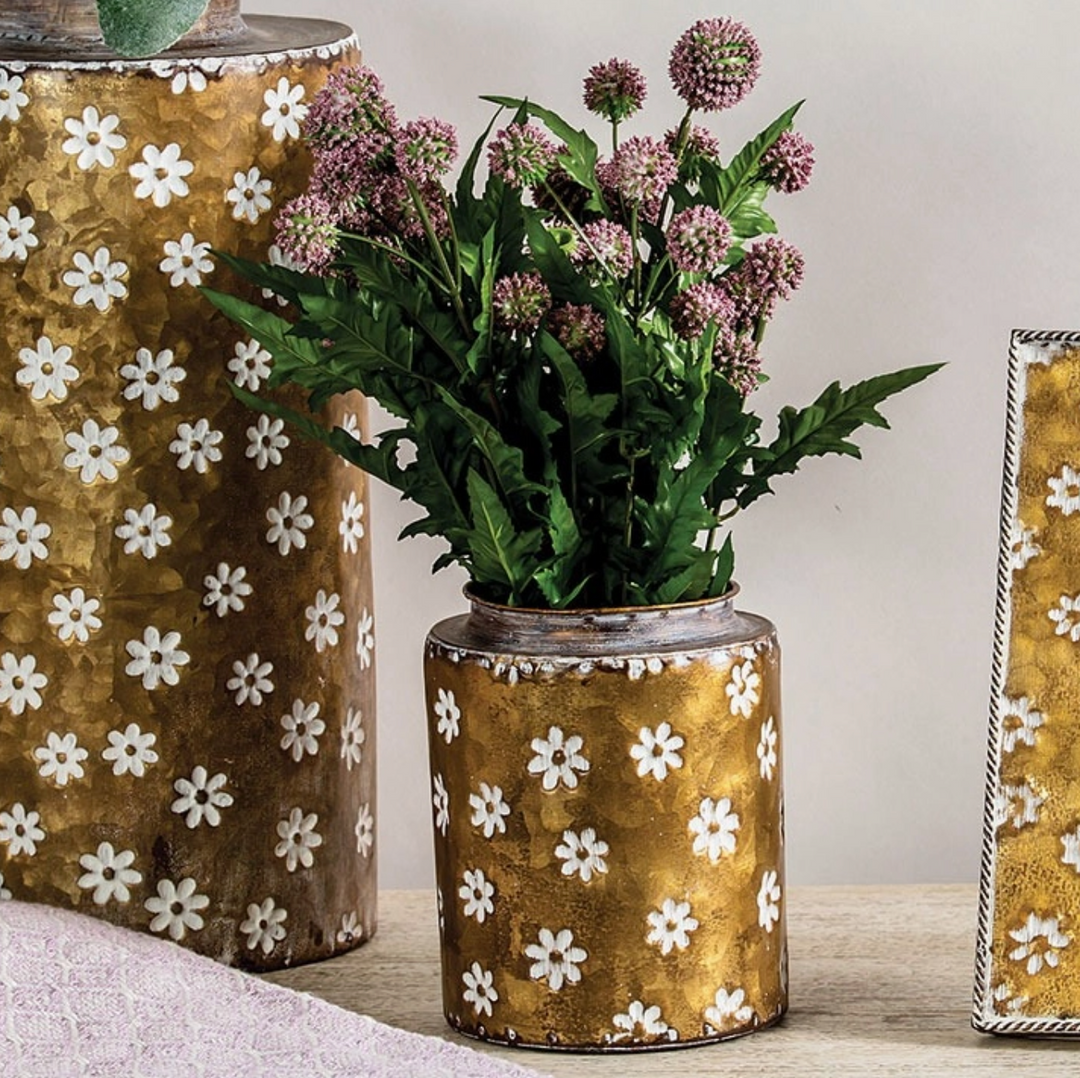 A brass vase with a floral pattern, displaying white flowers, placed on a book on a wooden surface.