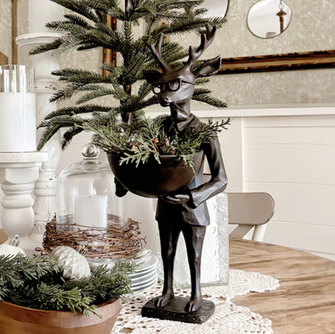 Decorative statue of a deer holding a bowl of greenery on a table with festive decorations.