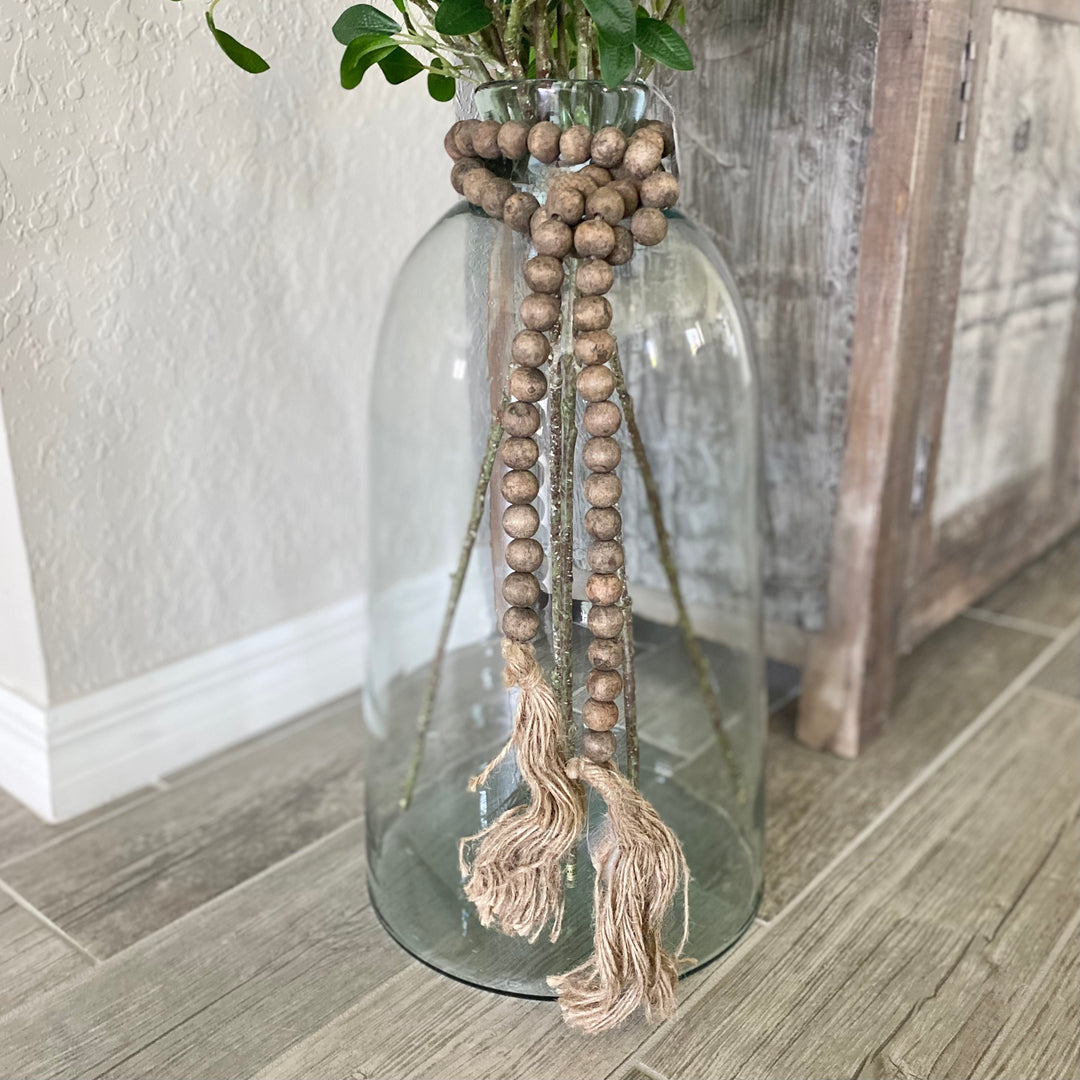 Glass vase with wooden beads and tassels on a wooden floor