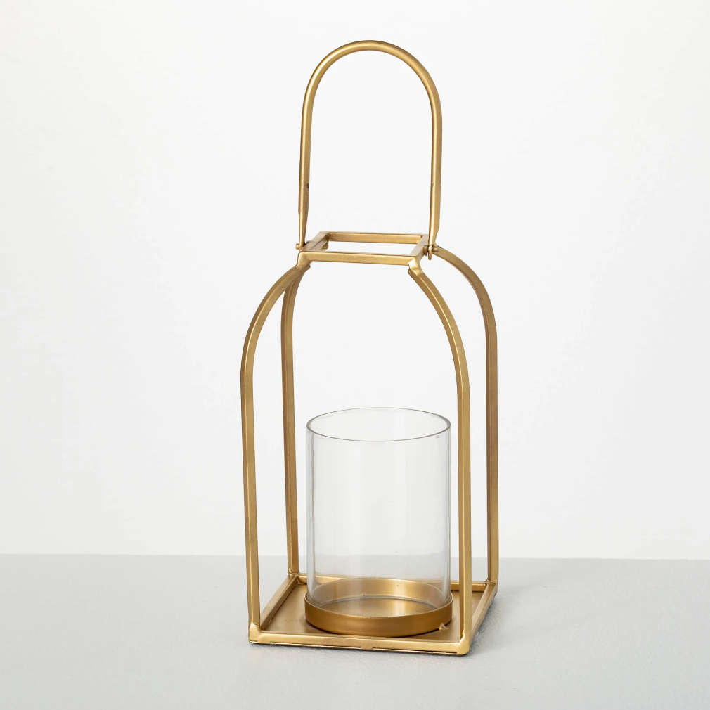 A brushed gold metal lantern candle holder with a clear glass hurricane liner.
