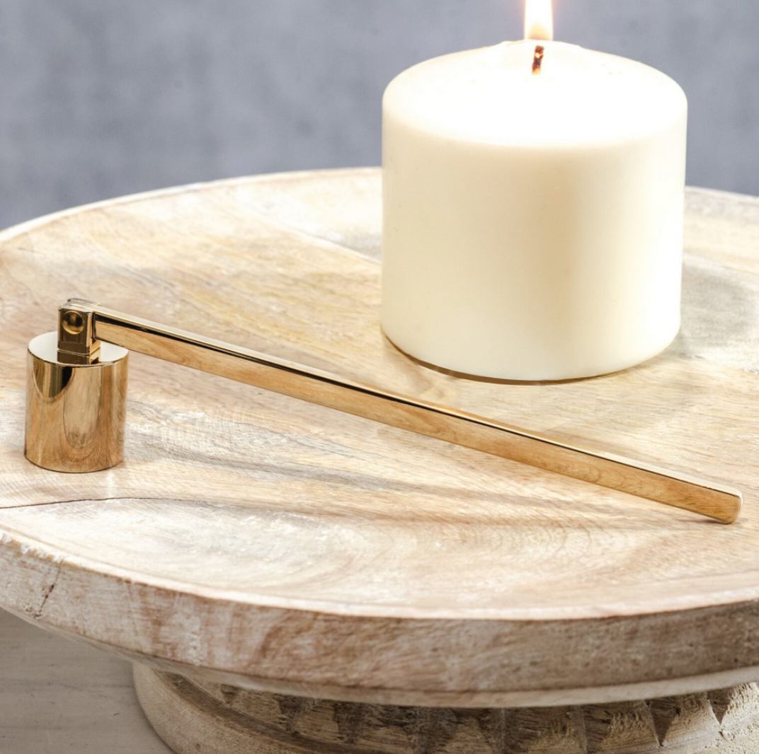 Gold candle snuffer on a wooden surface with a white candle