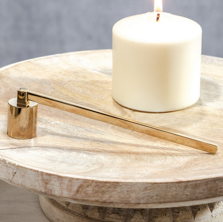 Gold candle snuffer on a wooden surface with a white candle