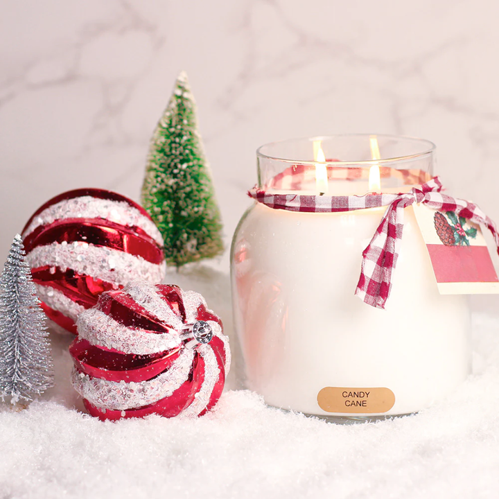 Candy Cane Scented Candle with a candy cane-themed label next to a candy cane ornament on a snowy surface.