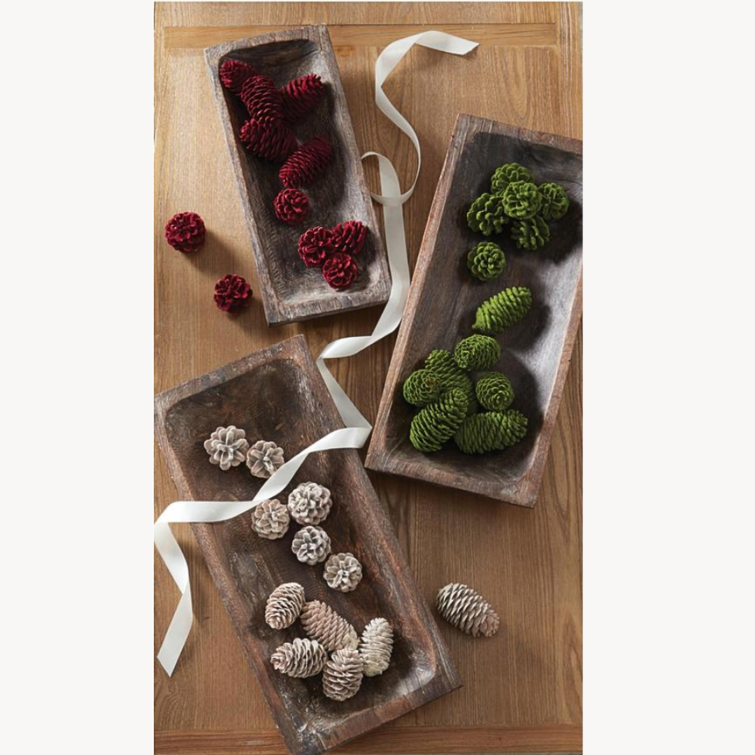 Three wooden trays with red, green, and white pine cones on a wooden surface.