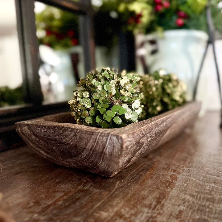 Decorative carved wooden tray with green spherical bowl fillers on a wooden surface