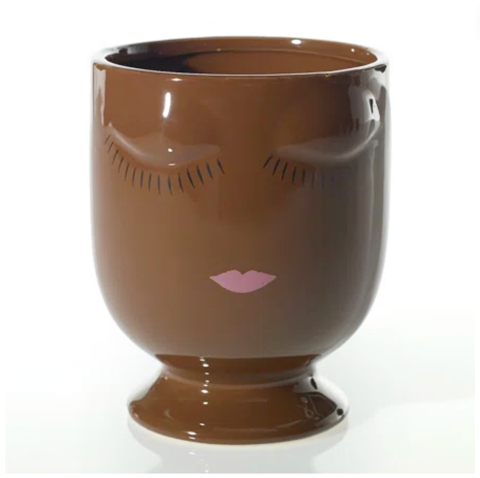 A brown ceramic planter with a cartoonish face design in brown and pink, on a plain background.