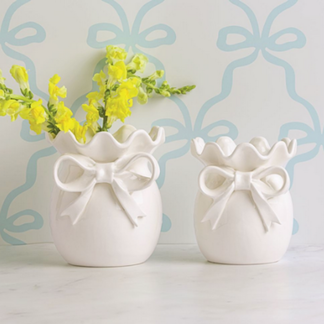 Two white ceramic vases with bow designs on a light blue background with decorative patterns.