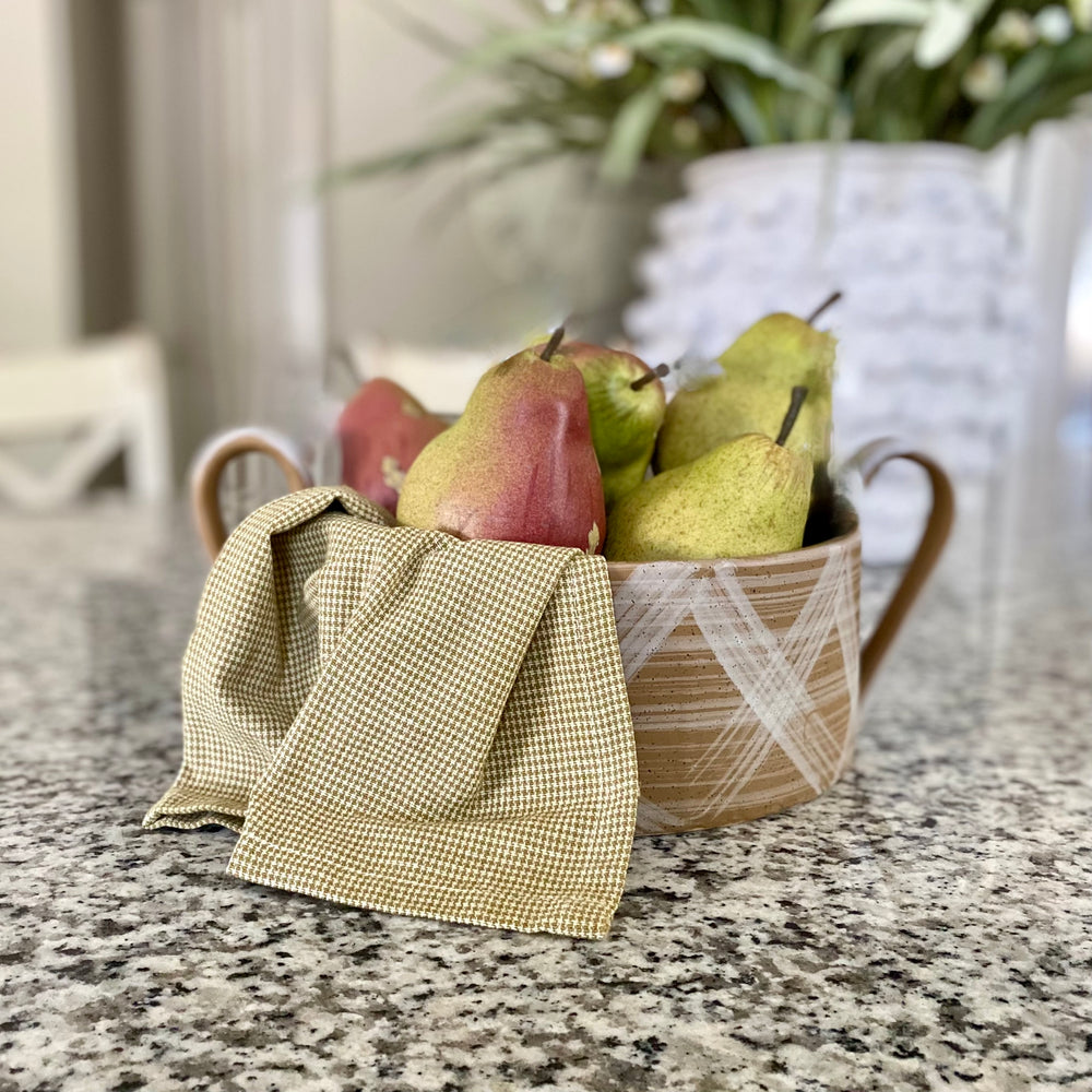 A ceramic Gracie Bowl with two-tone design, dark clay with hand-painted white glaze, displayed with pears inside it on a kitchen countertop.