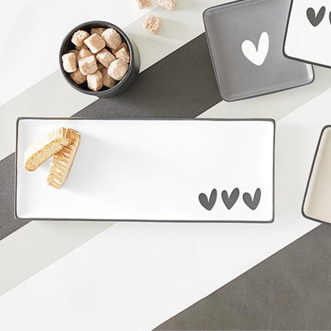 Rectangular ceramic plate with decorative cutouts on a white surface with cookies and a bowl.
